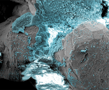 Blue bubbly material fills the middle and top of this microscope image. It shows the minerals created when sand is blasted with low voltage electricity in an attempt to sand into stone.